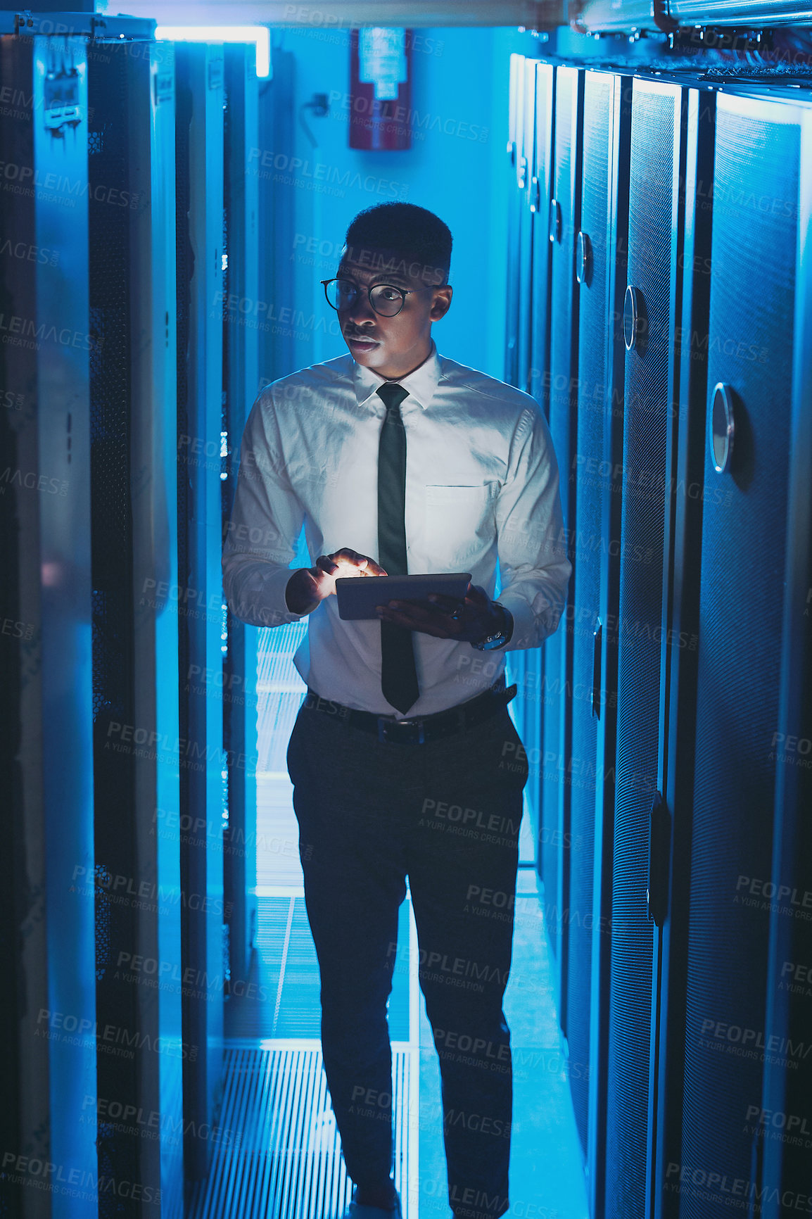 Buy stock photo Shot of a young IT specialist standing alone in the server room and using a digital tablet