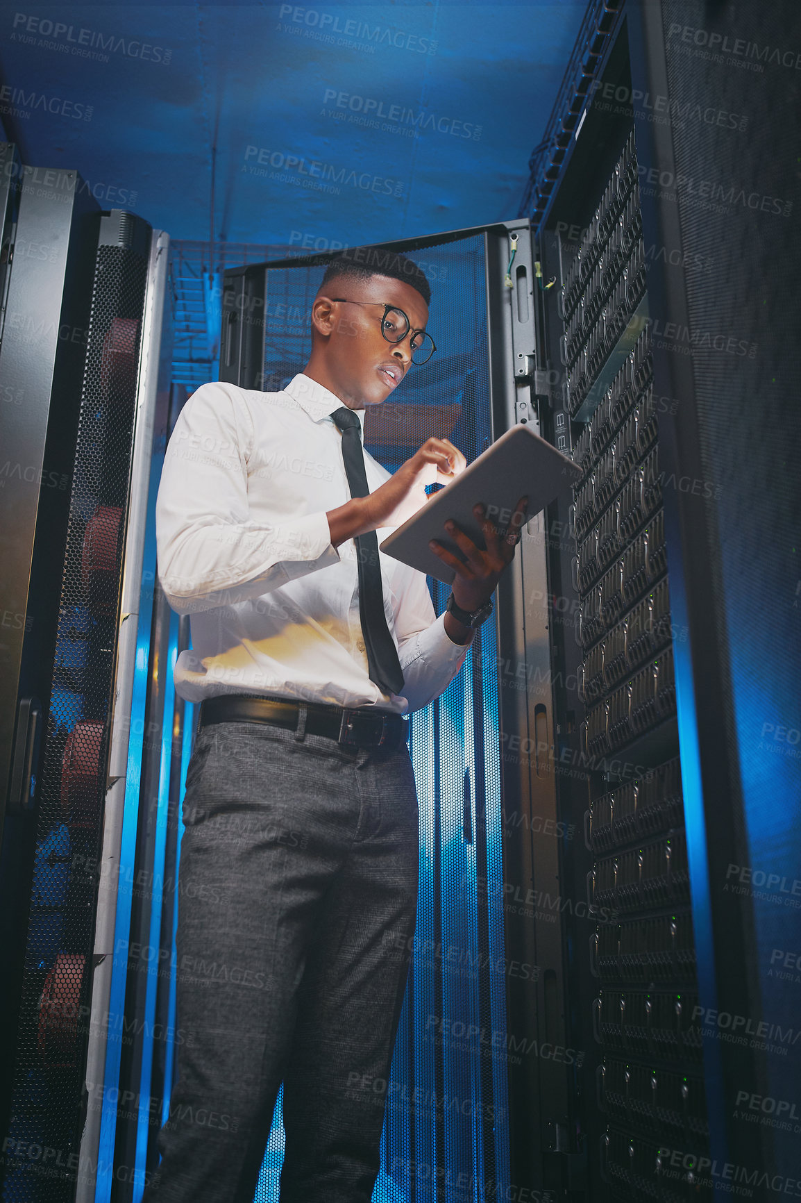 Buy stock photo Shot of a young IT specialist standing alone in the server room and using a digital tablet