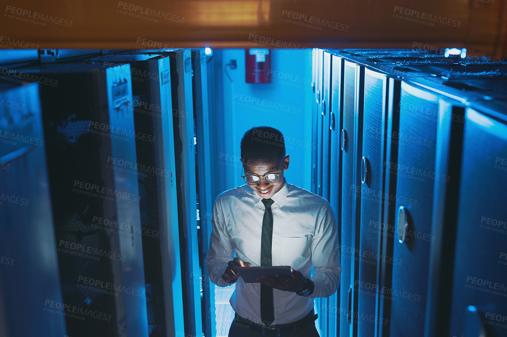 Buy stock photo Shot of a young IT specialist standing alone in the server room and using a digital tablet