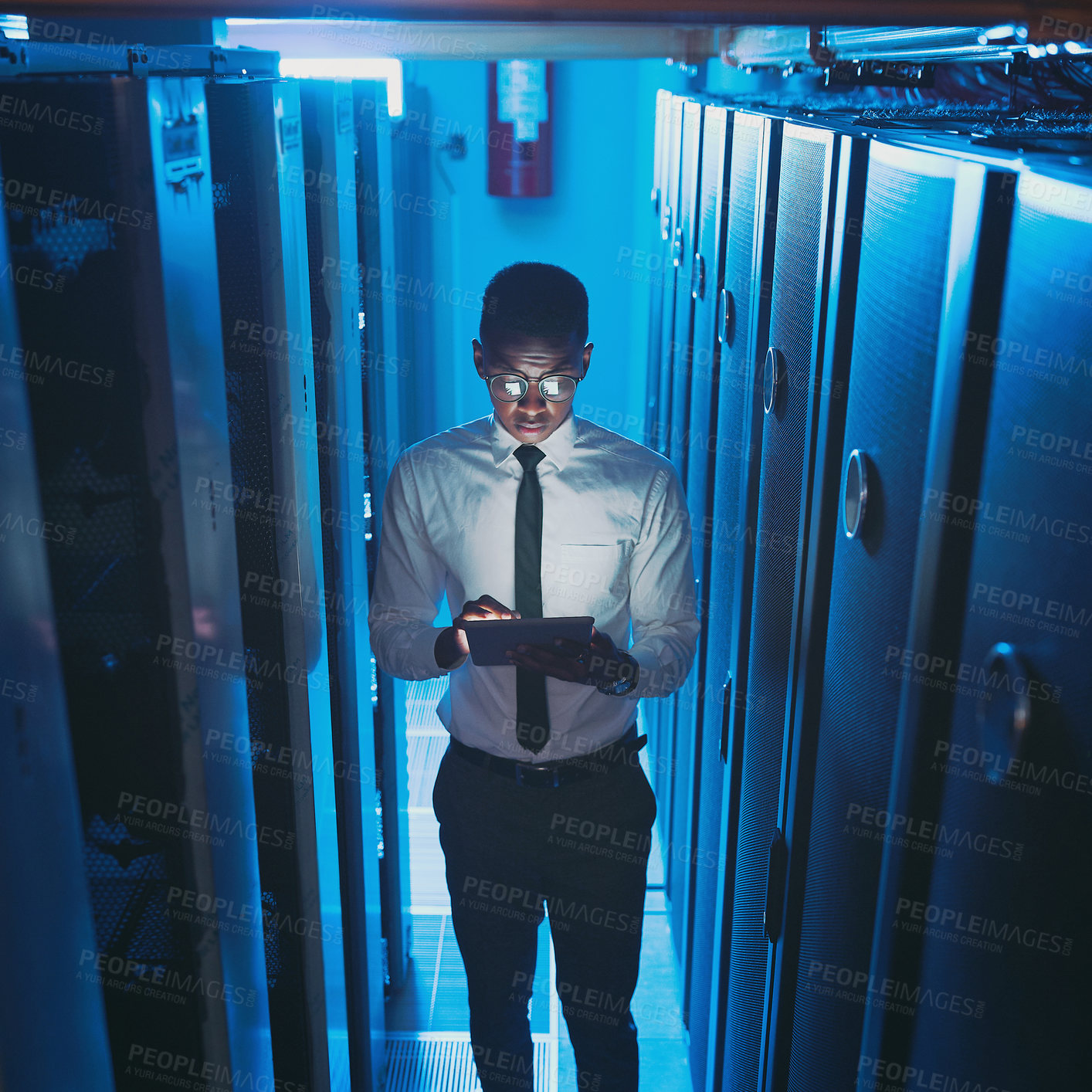 Buy stock photo Shot of a young IT specialist standing alone in the server room and using a digital tablet