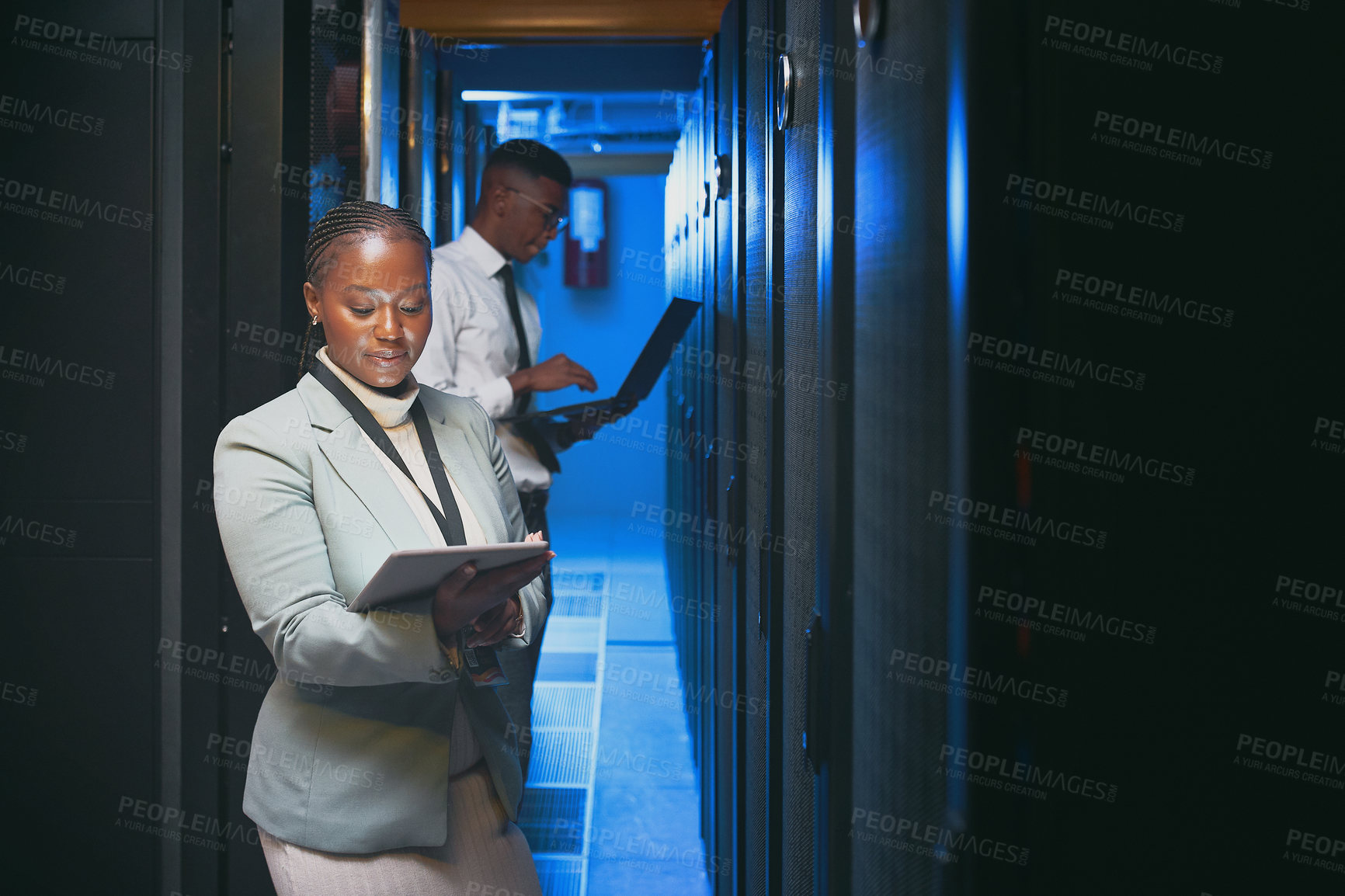 Buy stock photo Shot of two young IT specialists standing together in the server room and using technology