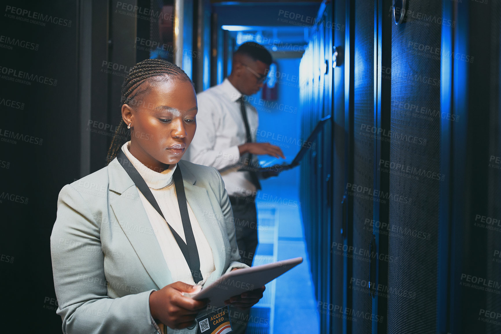 Buy stock photo Shot of two young IT specialists standing together in the server room and using technology