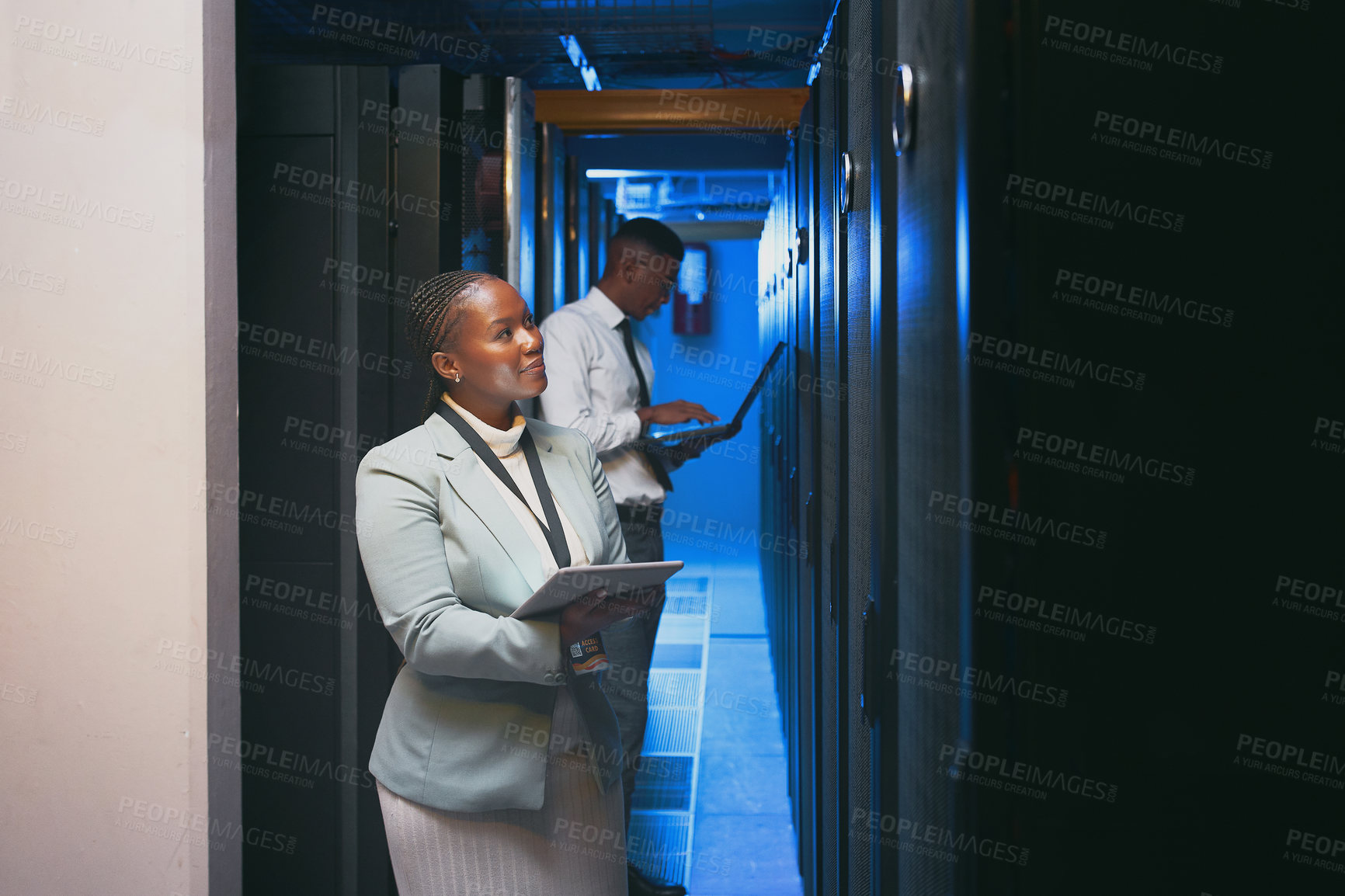 Buy stock photo Shot of two young IT specialists standing together in the server room and using technology