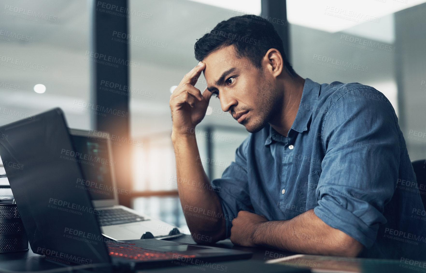 Buy stock photo Shot of a stressed young man using a laptop in a modern office