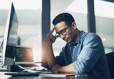 Buy stock photo Shot of a young man looking stressed while using a computer in a modern office
