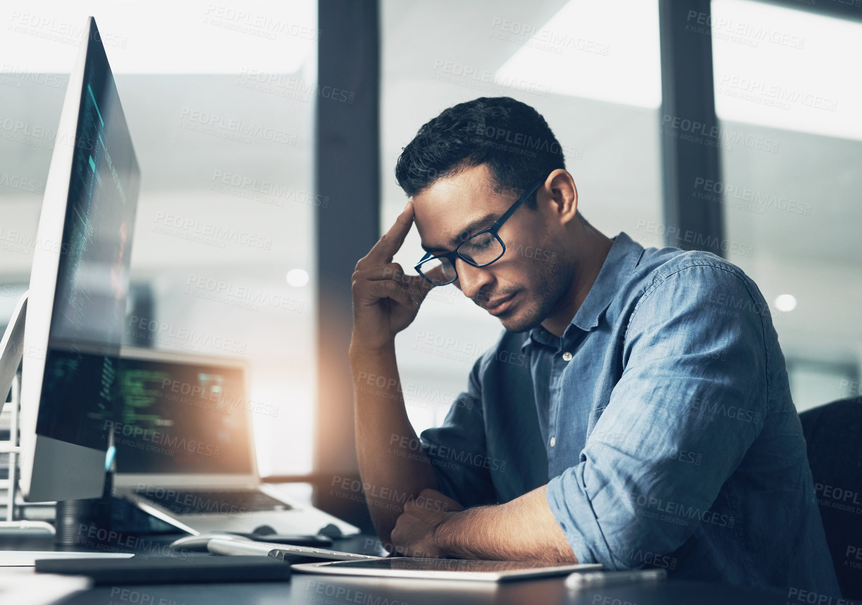 Buy stock photo Shot of a young man looking stressed while using a computer in a modern office