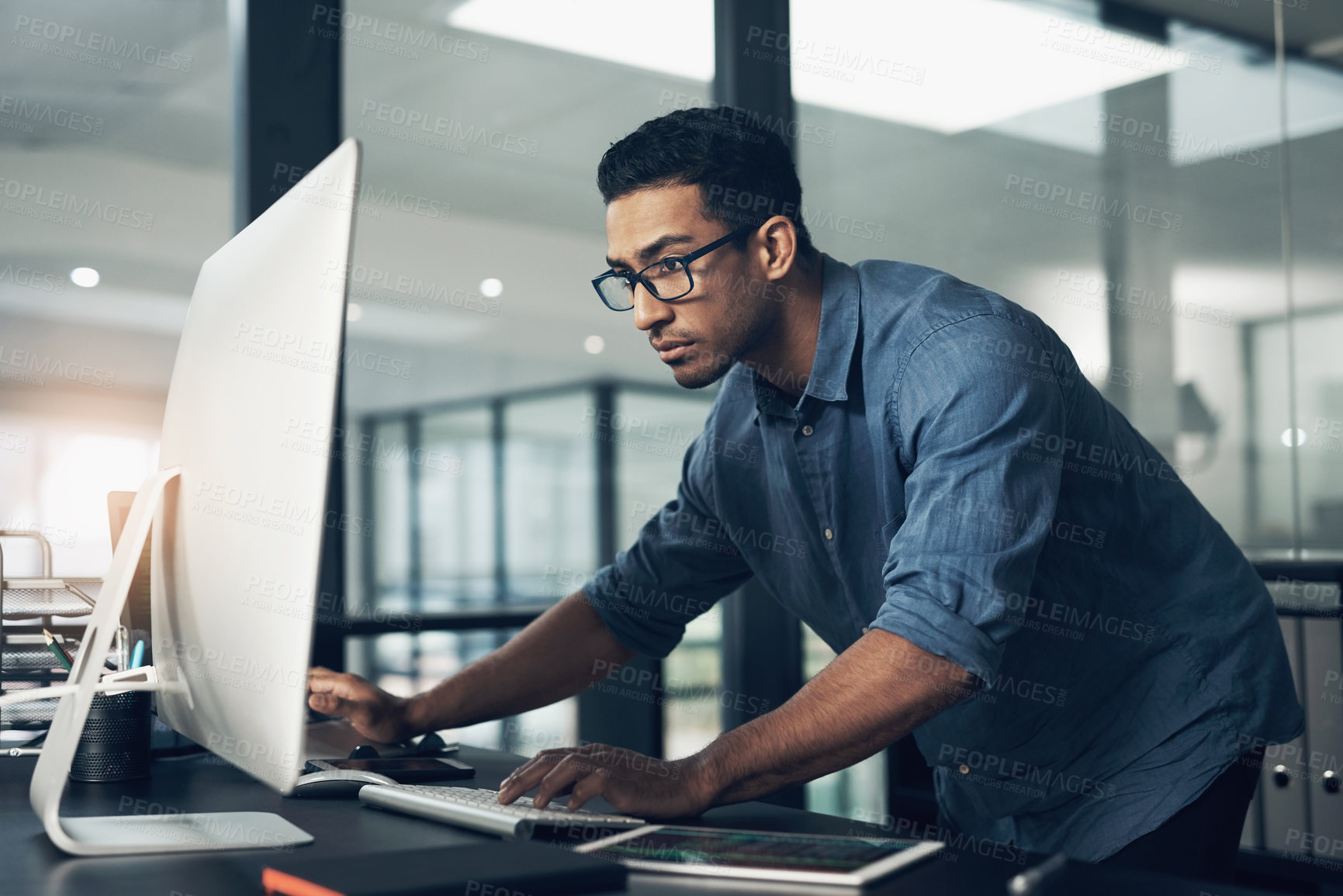 Buy stock photo Shot of a young man using a computer in a modern office