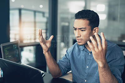 Buy stock photo Shot of a young frustrated man making hopeless gestures while using a laptop in a modern office