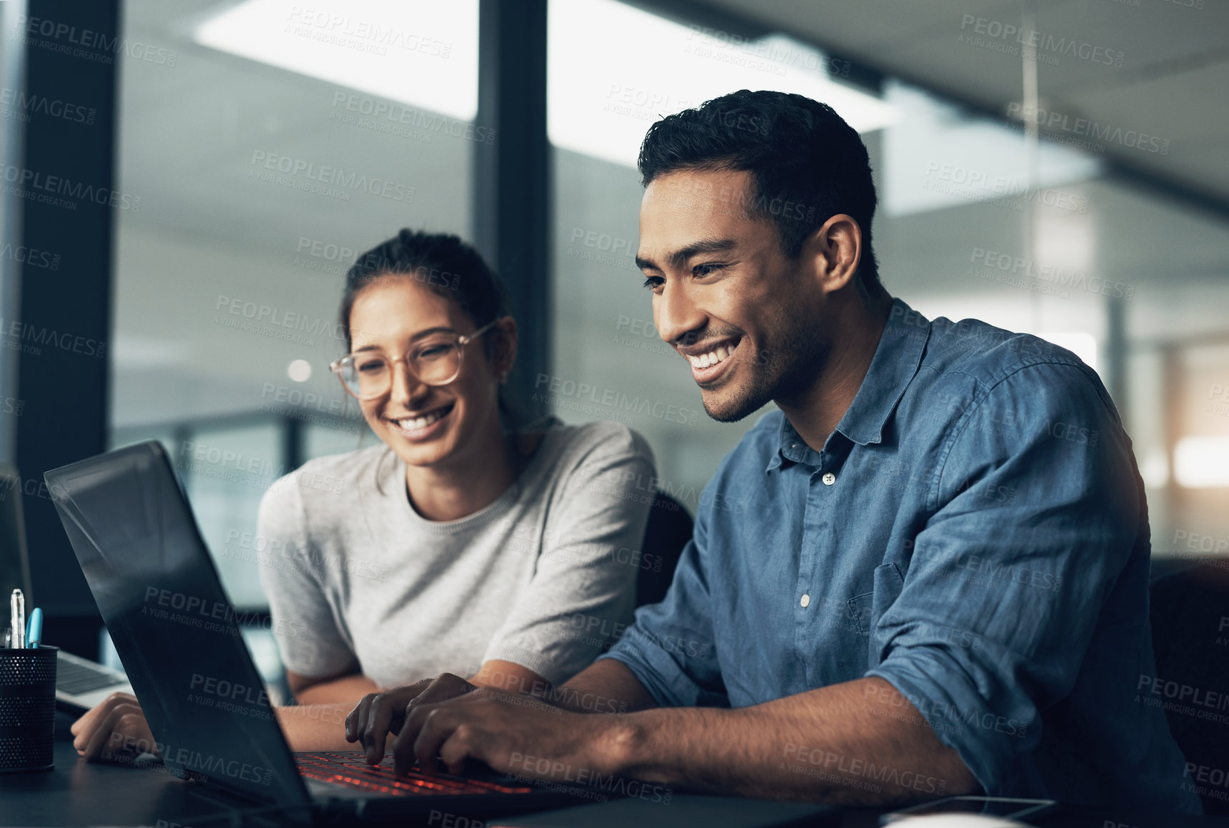 Buy stock photo Shot of two young workers using a laptop in a modern office