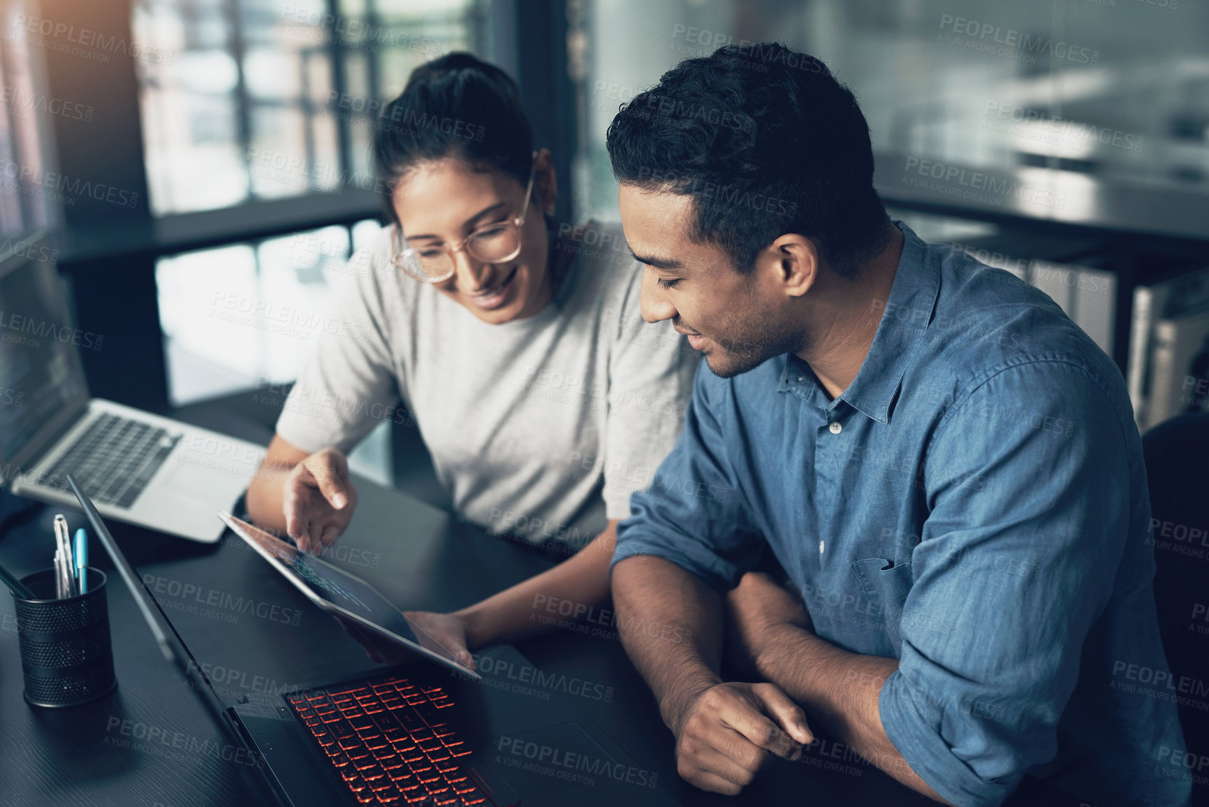 Buy stock photo Shot of two young workers using a digital tablet in a modern office