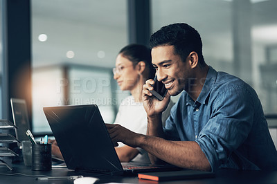 Buy stock photo Shot of a young man using his cellphone while working on a laptop in a modern office