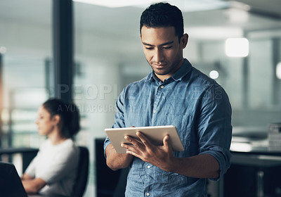 Buy stock photo Shot of a young man using a digital tablet in a modern office