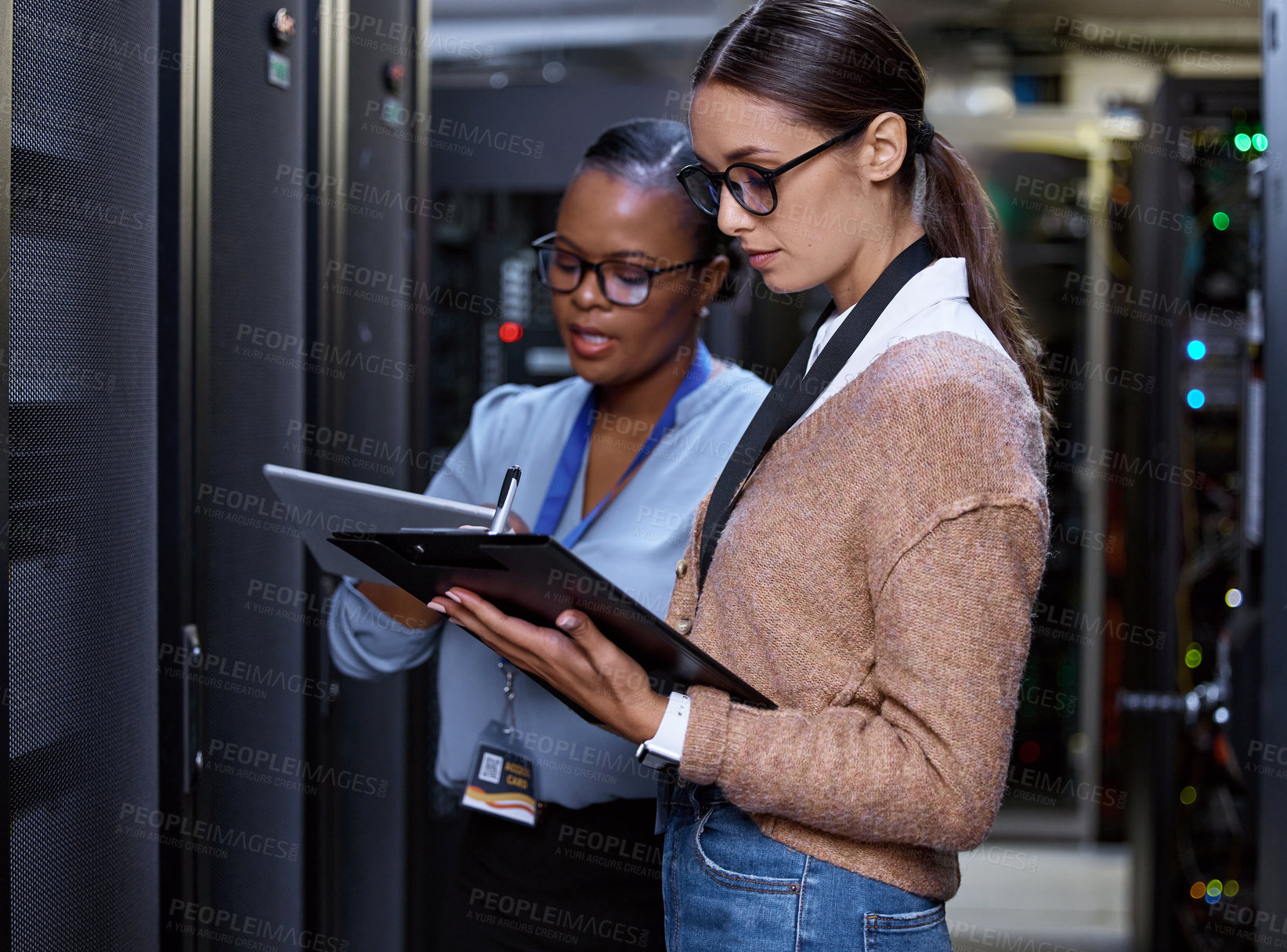 Buy stock photo Cropped shot of two attractive young female computer programmers working together in a server room