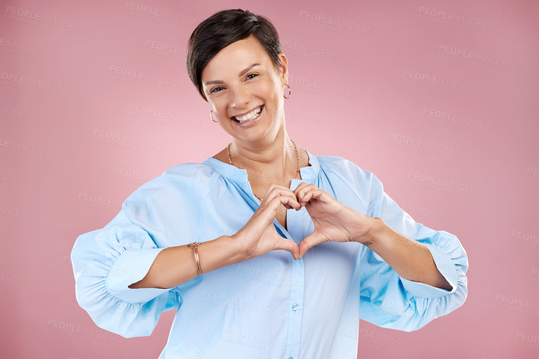 Buy stock photo Cropped portrait of an attractive young woman making a heart shape with her hands in studio against a pink background