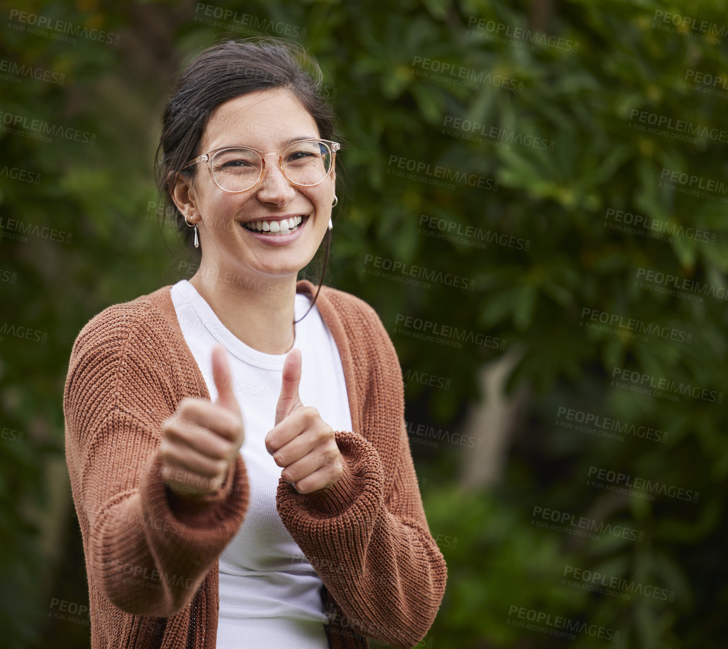 Buy stock photo Portrait of a cheerful young woman showing thumbs up outdoors