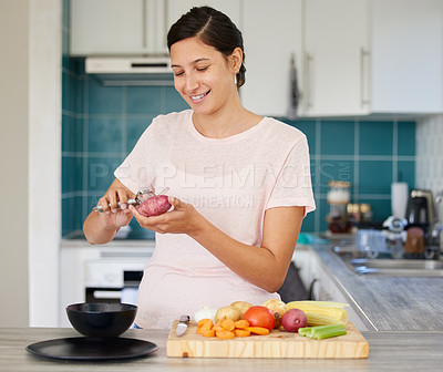 Buy stock photo Shot of a young woman peeling a potato in her kitchen