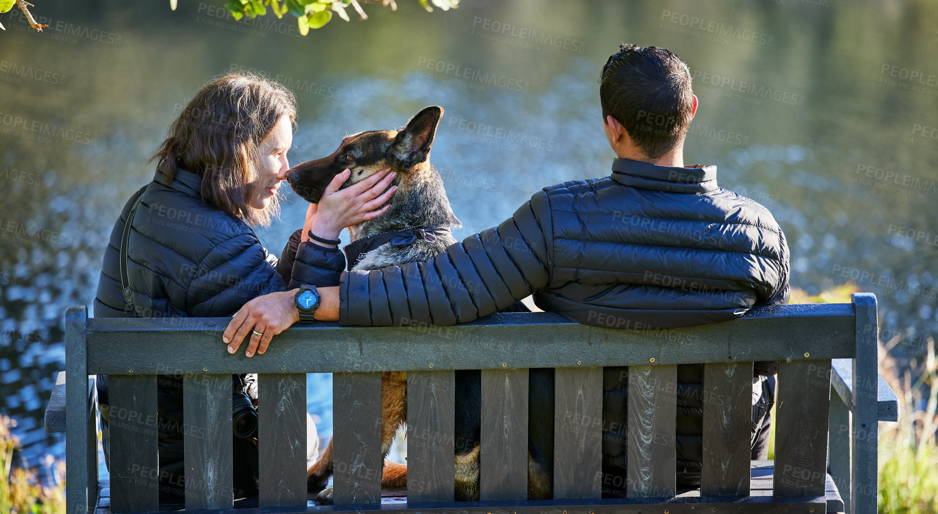 Buy stock photo Couple, dog and back on park bench, outdoor and relax by lake for connection, care or touch on holiday. Man, woman and pet animal by water with German shepherd for trust, vacation or nature in winter