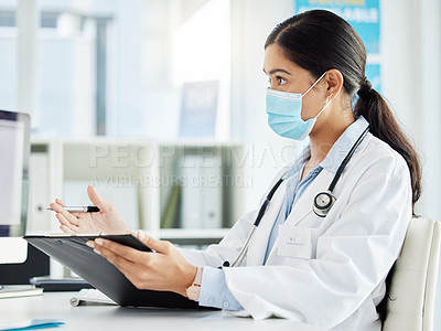 Buy stock photo Shot of a doctor wearing a face mask while sitting and talking in her clinic during a consult