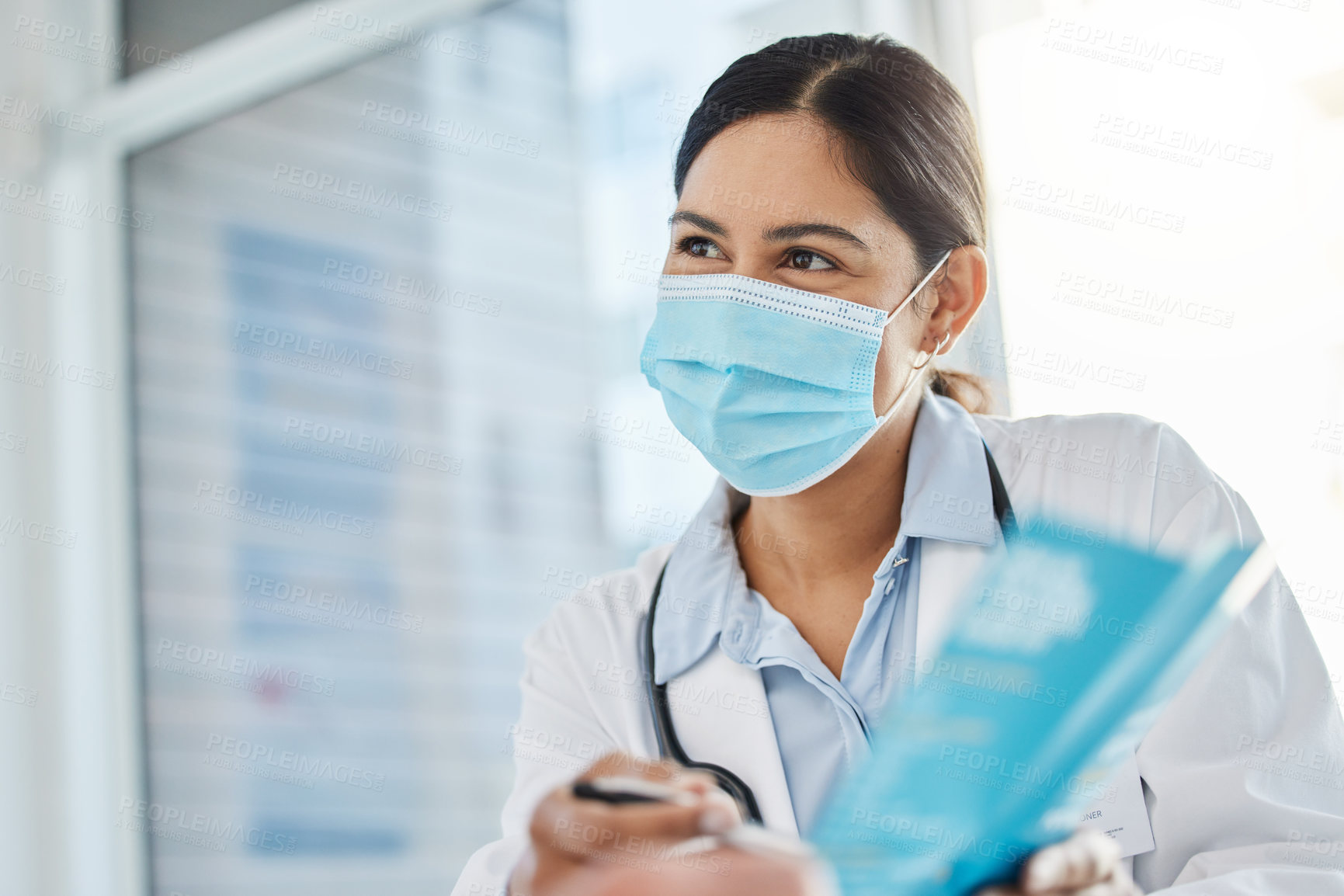 Buy stock photo Shot of doctor wearing a face mask and giving a leaflet to her patient during a consult in the clinic