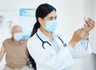 Buy stock photo Shot of a doctor standing and using a syringe to draw out the Covid vaccine in her clinic