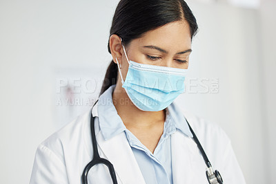 Buy stock photo Shot of a doctor wearing a face mask and standing alone in her clinic during the day