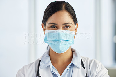 Buy stock photo Shot of a doctor wearing a face mask and standing alone in her clinic during the day
