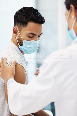Buy stock photo Shot of a young man sitting and wearing a face mask while getting his Covid vaccine in the clinic