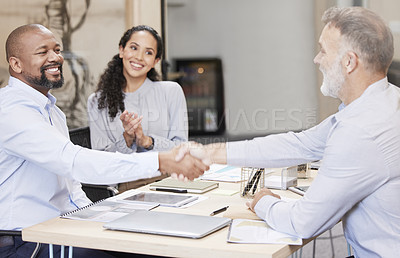 Buy stock photo Cropped shot of two handsome mature businessmen shaking hands while sitting in the boardroom during a meeting