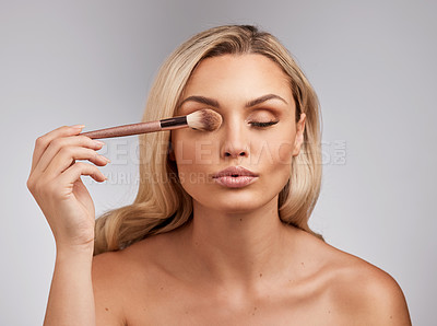 Buy stock photo Studio shot of a beautiful young woman holding a makeup brushe against a grey background