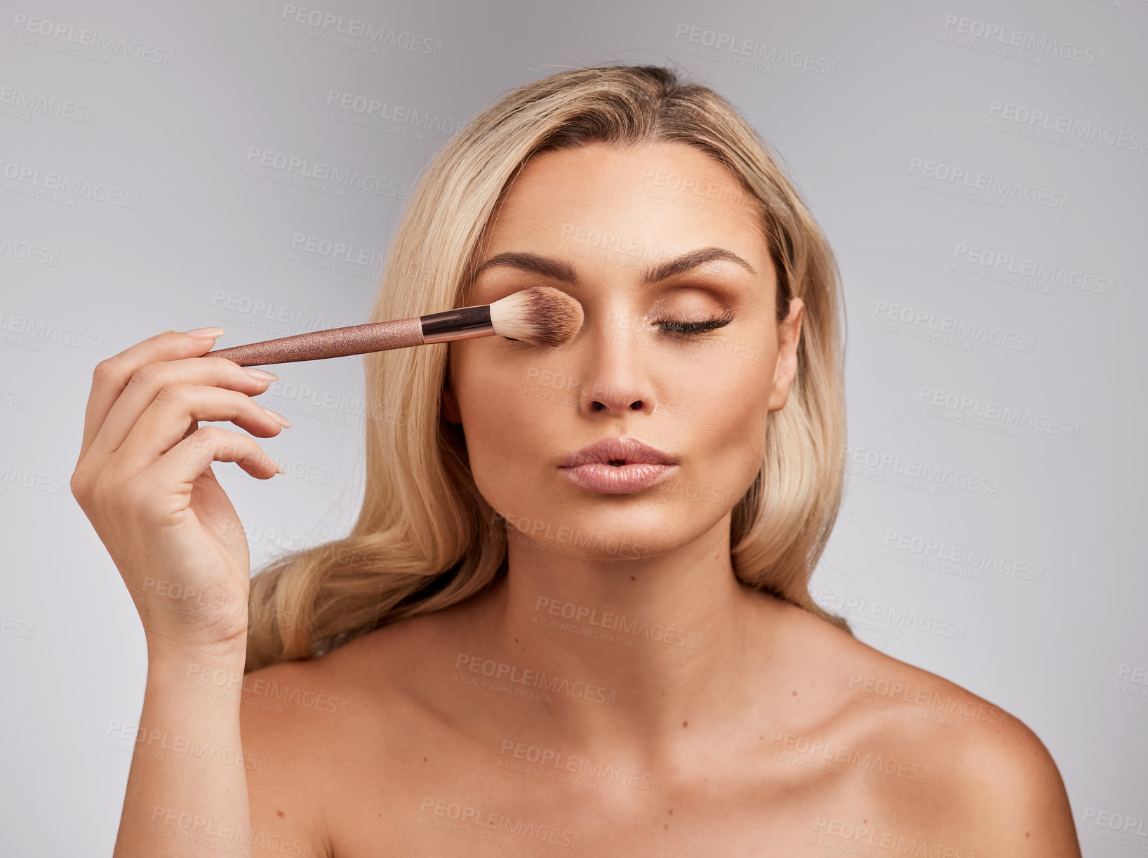 Buy stock photo Studio shot of a beautiful young woman holding a makeup brushe against a grey background