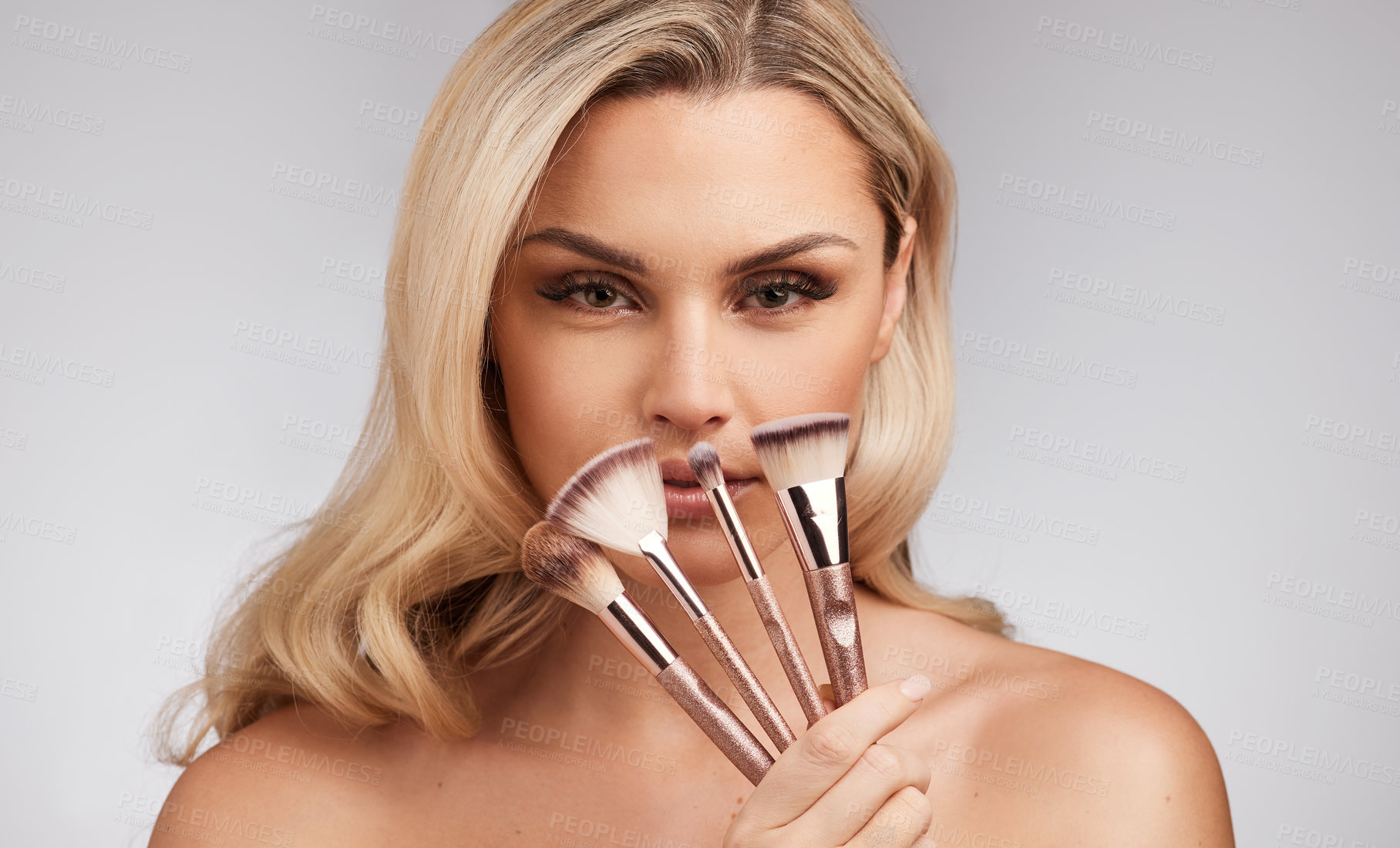 Buy stock photo Studio portrait of a beautiful young woman holding a set of makeup brushes against a grey background