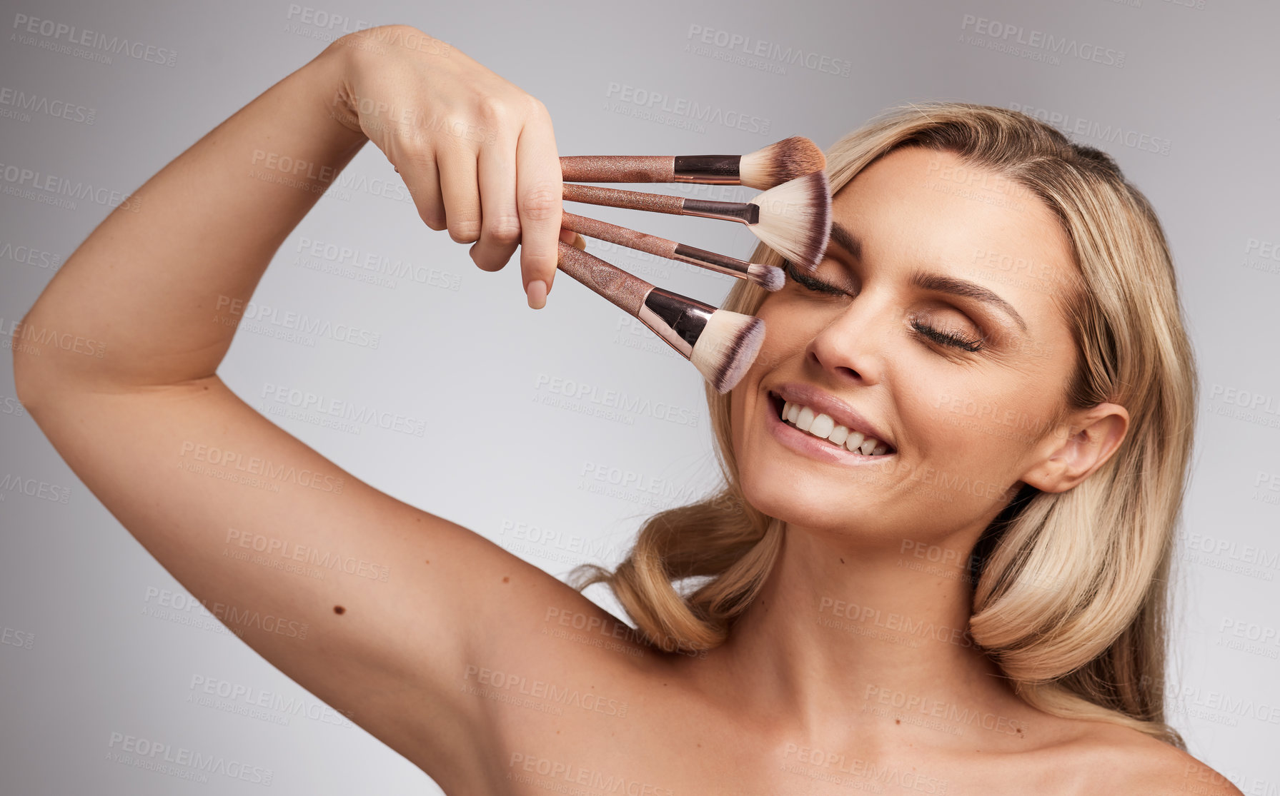 Buy stock photo Studio portrait of a beautiful young woman holding a set of makeup brushes against a grey background