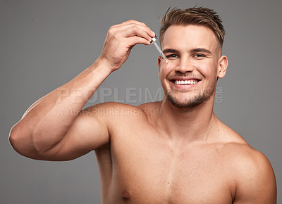 Buy stock photo Studio shot of a handsome young man applying serum to his face against a grey background