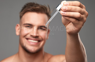 Buy stock photo Studio shot of a handsome young man applying serum to his face against a grey background