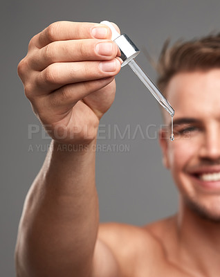 Buy stock photo Studio shot of a handsome young man applying serum to his face against a grey background