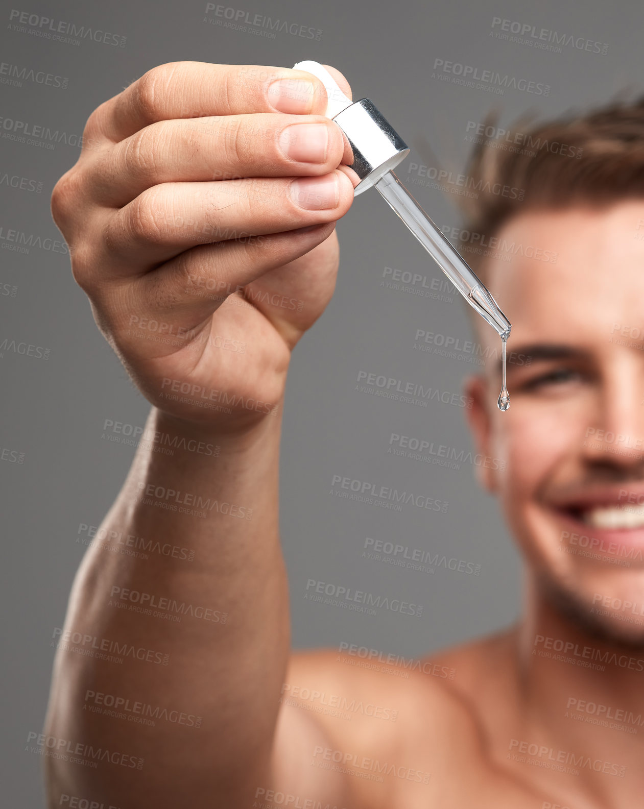 Buy stock photo Studio shot of a handsome young man applying serum to his face against a grey background