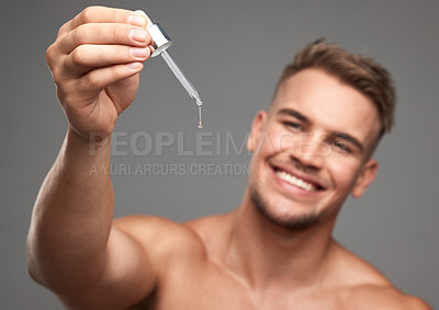 Buy stock photo Studio shot of a handsome young man applying serum to his face against a grey background