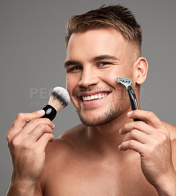 Buy stock photo Studio shot of a handsome young man holding a razor and brush against a grey background