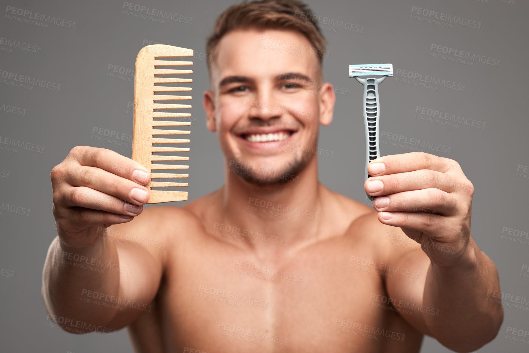 Buy stock photo Studio shot of a handsome young man holding a comb and shaving brush against a grey background