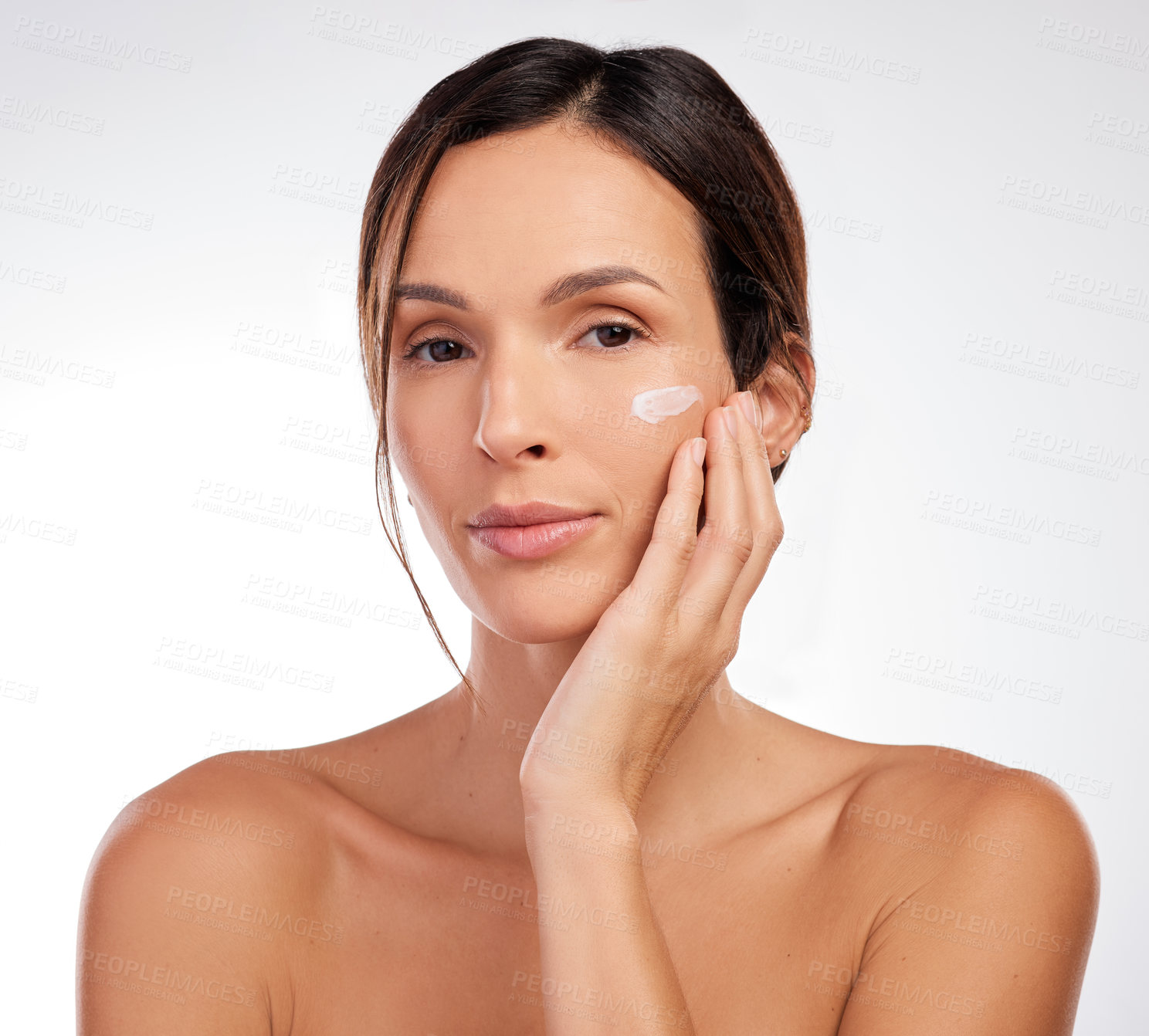 Buy stock photo Shot of an attractive young woman applying moisturiser to her face in the studio