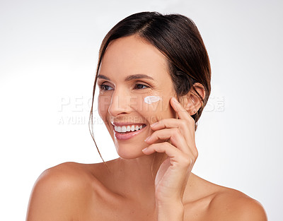 Buy stock photo Shot of an attractive young woman applying moisturiser to her face in the studio