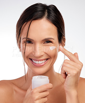 Buy stock photo Shot of an attractive young woman applying moisturiser to her face in the studio