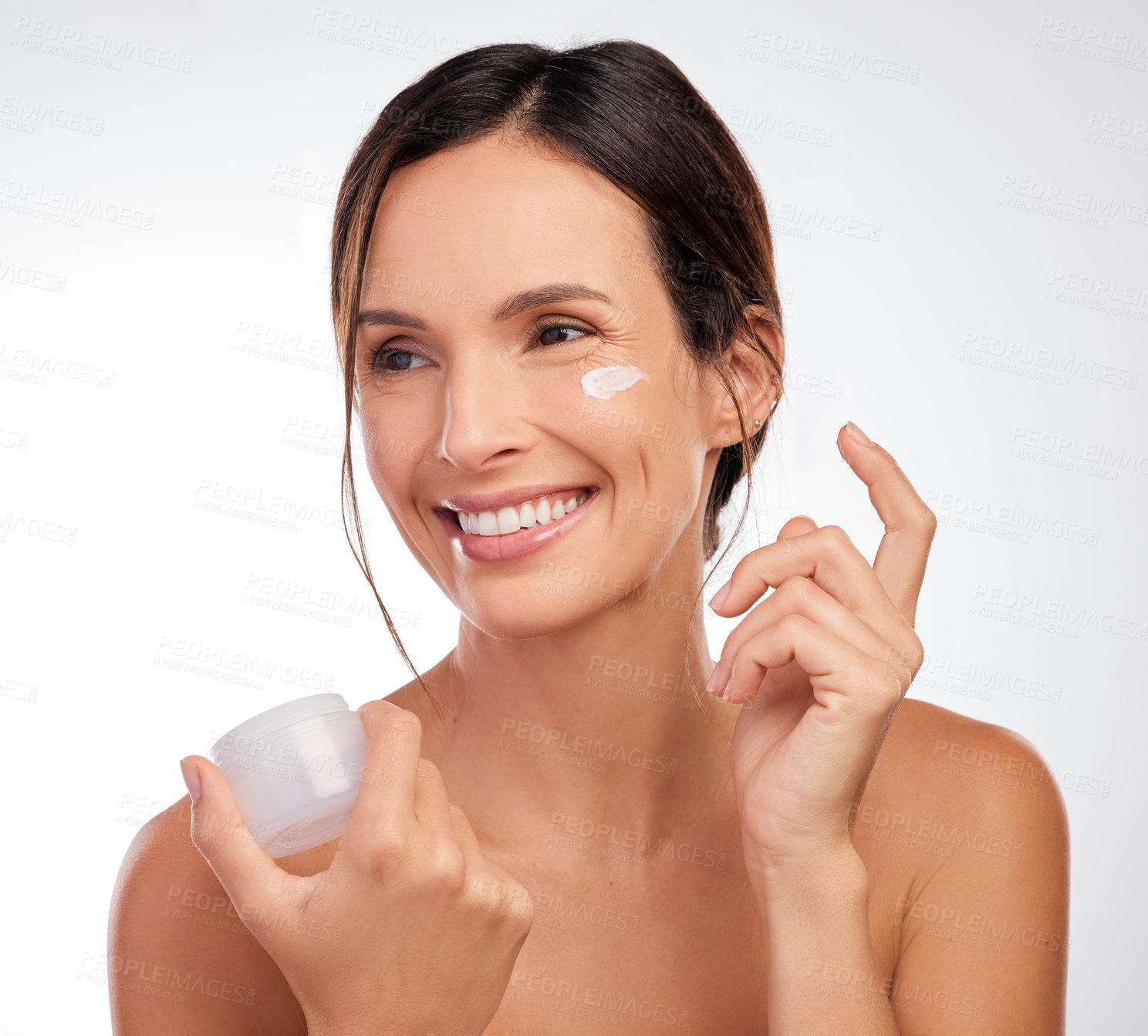 Buy stock photo Shot of an attractive young woman applying moisturiser to her face in the studio