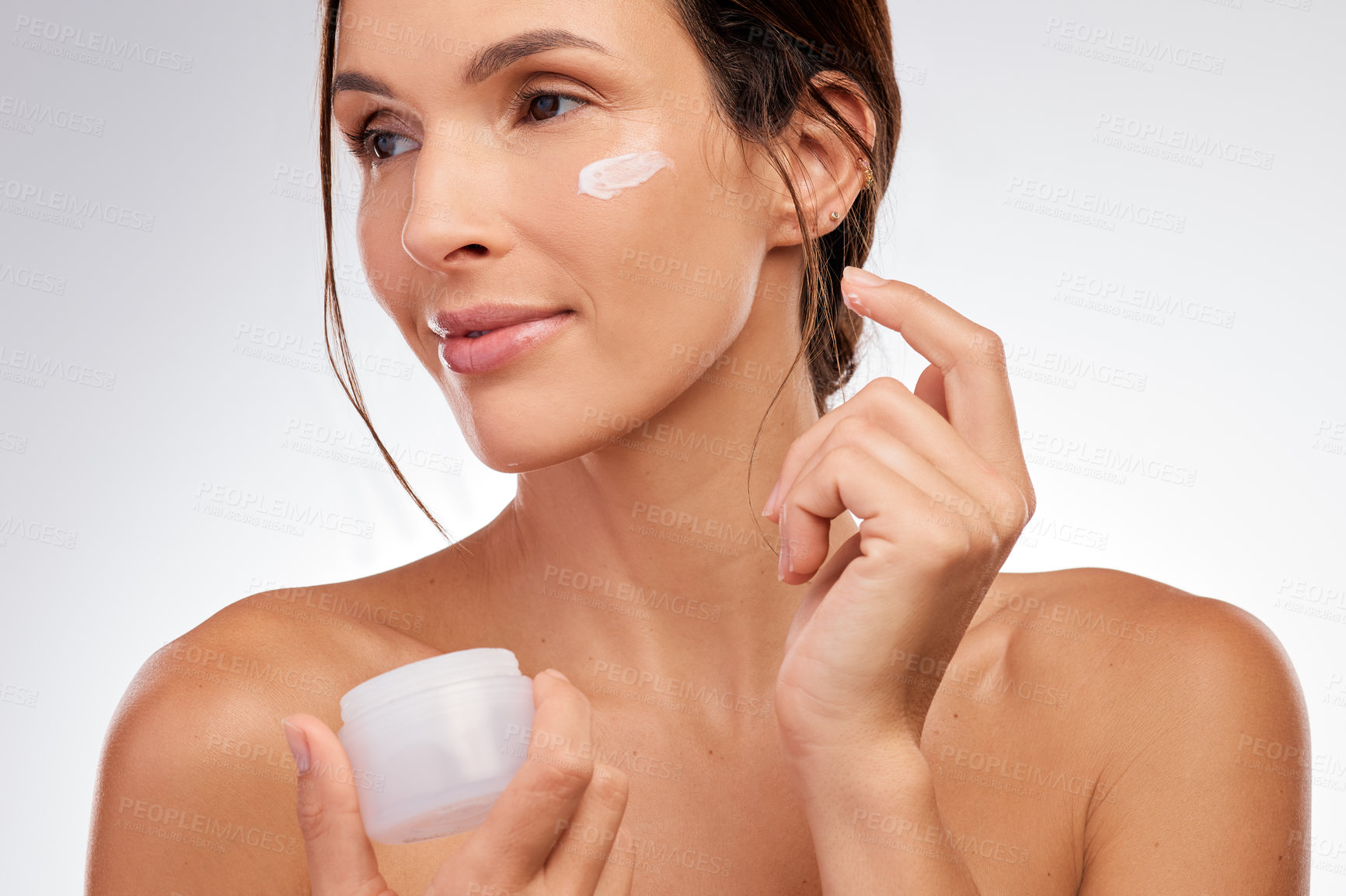 Buy stock photo Shot of an attractive young woman applying moisturiser to her face in the studio