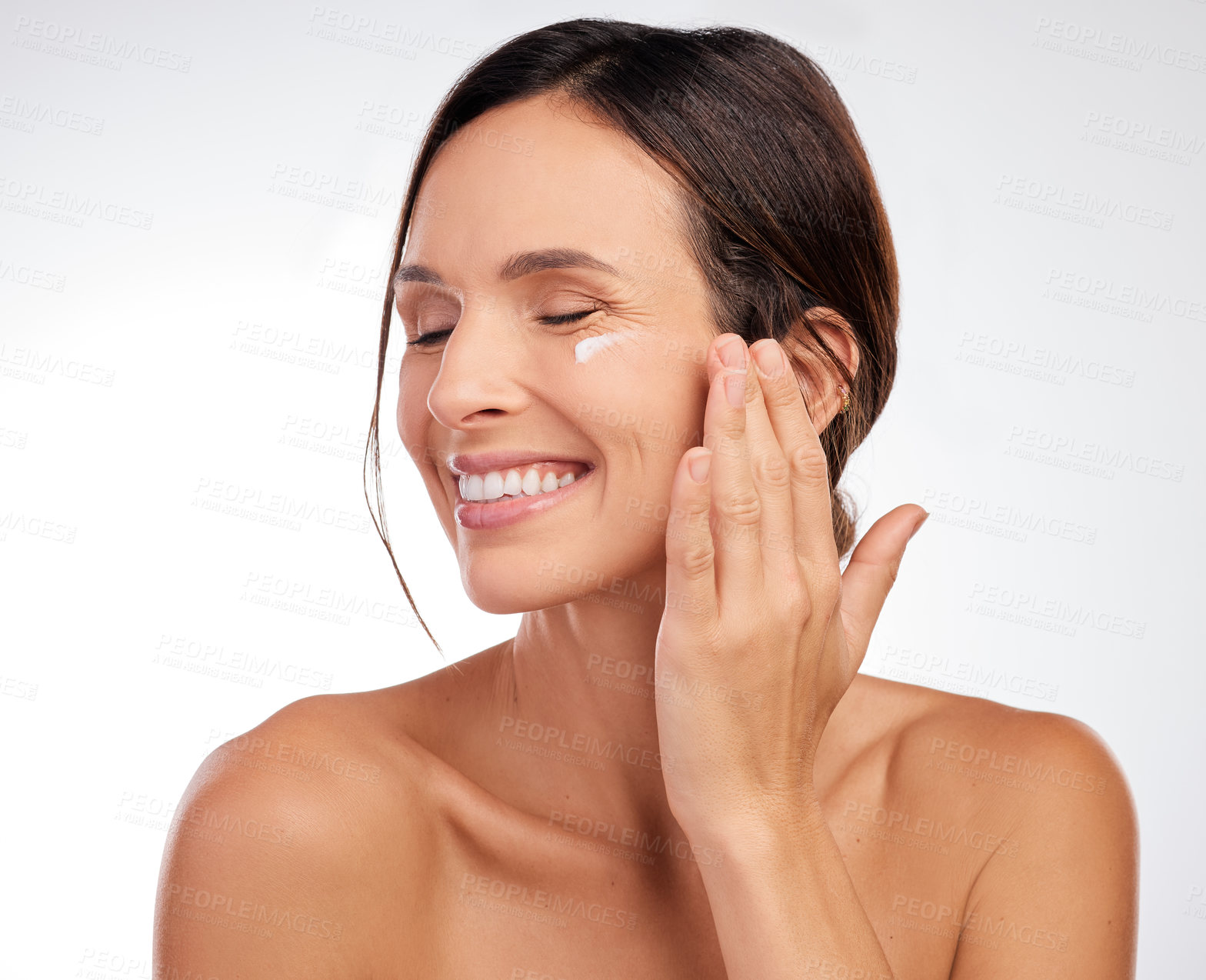 Buy stock photo Shot of an attractive young woman applying moisturiser to her face in the studio