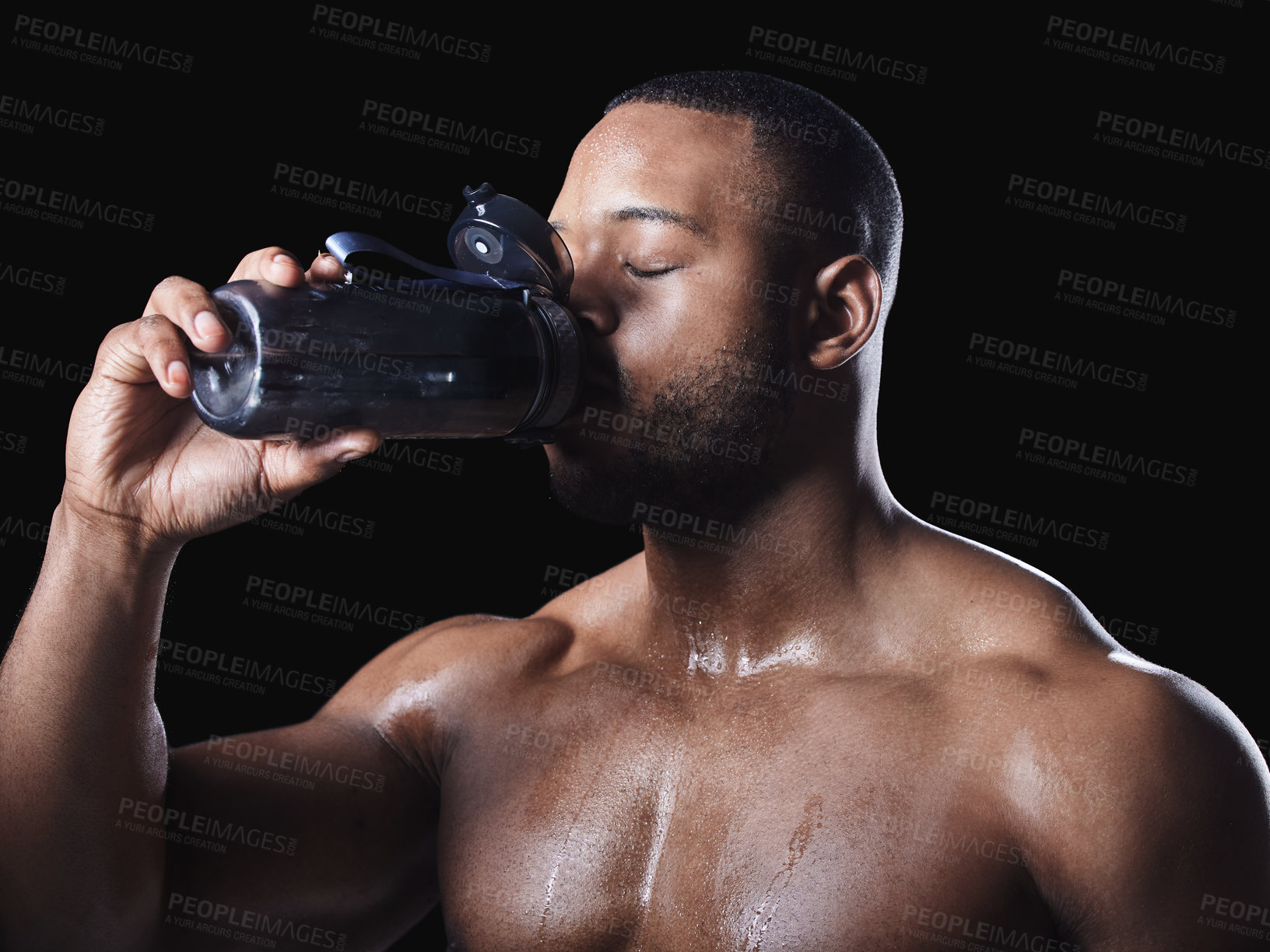 Buy stock photo Studio shot of a young fit man drinking water after exercising against a black background