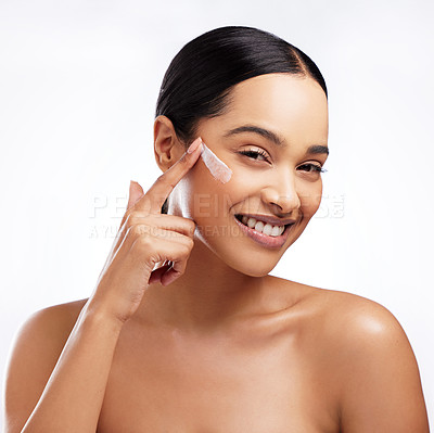 Buy stock photo Studio portrait of a beautiful young woman applying moisturiser to her face against a white background