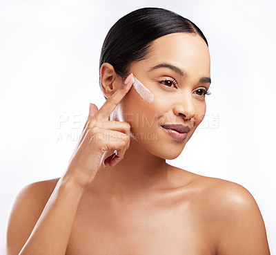 Buy stock photo Studio shot of a beautiful young woman applying moisturiser to her face against a white background