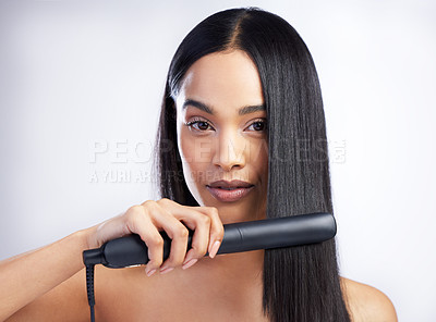 Buy stock photo Shot of an attractive young woman standing alone in the studio and styling her hair with a hair straightener