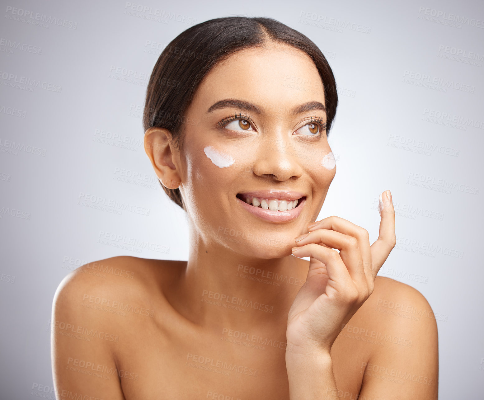 Buy stock photo Studio shot of an attractive young woman applying moisturiser to her face against a grey background